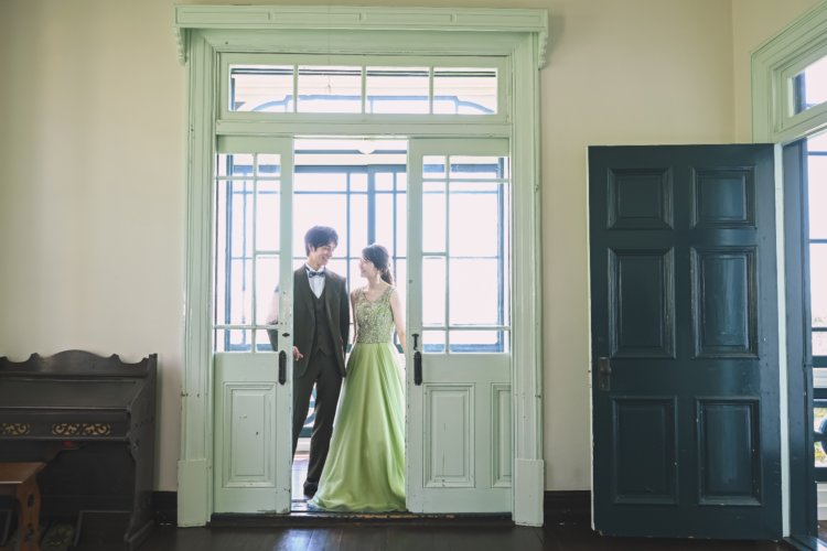 緑の可愛い扉の前で見つめ合う夫婦の結婚写真