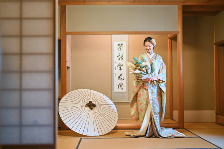 むらさき亭の和室の中で和傘と一緒に映る新婦の写真