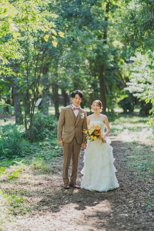 緑に囲まれた公園の小道に並んで立つ新郎新婦。ティアードのウェディングドレスで撮るナチュラルな前撮り