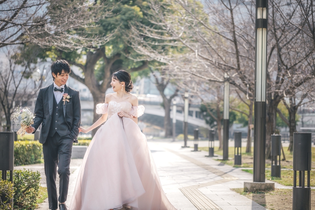 ピンクのドレスを着た新婦とタキシード姿の新郎が2人で歩いている写真