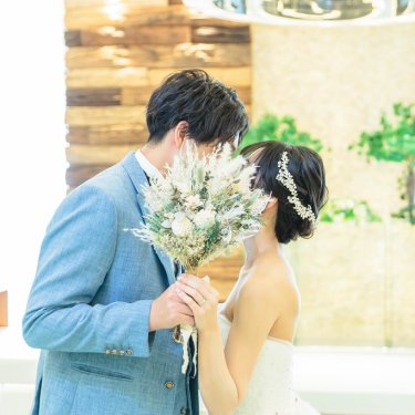 ドライフラワーのブーケで顔を隠してキスをする水色のスーツの新郎と花嫁。チャペルフォトの顔隠し