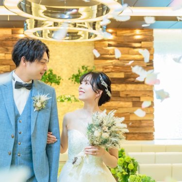 花びらが舞うチャペルで見つめ合う水色のスーツの新郎とドライフラワーのブーケの花嫁のチャペルフォト