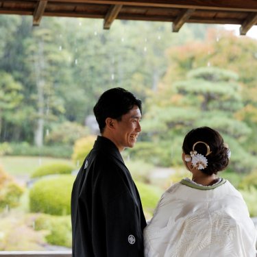 雨の大仙公園の東屋から庭を眺めて笑う紋付袴の新郎と白無垢の花嫁。雨の日に撮る和装前撮り