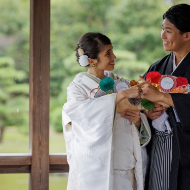 大仙公園の東屋で夫と妻の扇子を手に笑い合う紋付袴の新郎と白無垢の花嫁。和装ロケーションフォト
