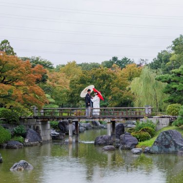 池と石橋が広がる大仙公園の日本庭園で和傘を差す新郎新婦を遠くから撮った和装ロケーションフォト