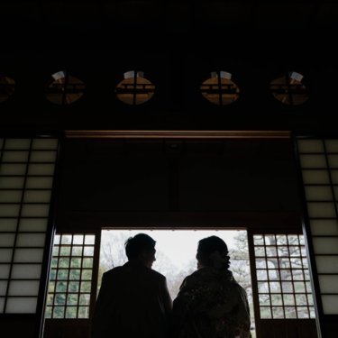 大仙公園にて、丸い欄間の座敷で、開けた障子の外を眺めて並ぶ新郎新婦のシルエット。光と影が美しい和装ロケーションフォト