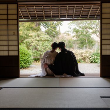 慶沢園にて、広い座敷の奥、開け放った戸の先の庭を眺めて寄り添う新郎新婦の後ろ姿のシルエット。和装前撮りの構図