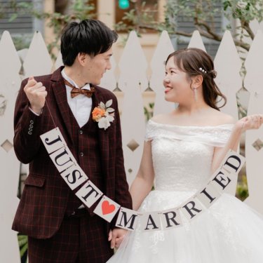 白い柵の前でJUST MARRIEDのガーランドを持つチェックのスーツの新郎と花嫁。神戸の洋装前撮り
