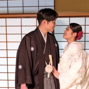 障子の前で寄り添い、見つめ合ってほほえむ紋付袴の新郎と白無垢の花嫁のアップ。慶沢園の和室で撮る和装前撮り
