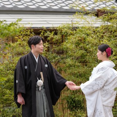 竹林と瓦屋根を背に、手を差し伸べて向き合う紋付袴の新郎と白無垢の花嫁。慶沢園で撮る和装前撮り