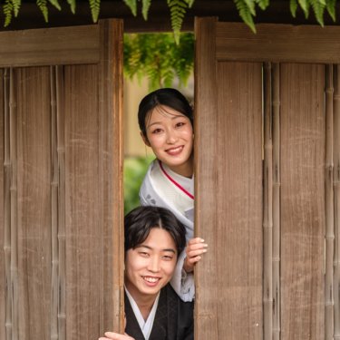 慶沢園にて、板塀の戸の隙間から縦に並んで顔をのぞかせ、笑う白無垢の花嫁と紋付の新郎。遊び心のある和装前撮り