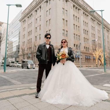 旧居留地のレトロなビルの前でサングラスとレザージャケットを合わせた新郎新婦。個性派の洋装前撮り