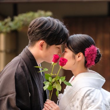 赤いバラの花を手に、鼻先を寄せ合う紋付の新郎と白無垢の花嫁のアップ。日本庭園で撮る和装前撮り