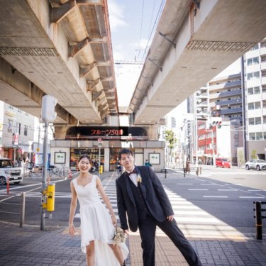 高架下の横断歩道で足を上げておどける新郎とショート丈のウェディングドレスの花嫁、遊び心のある街ロケ前撮り