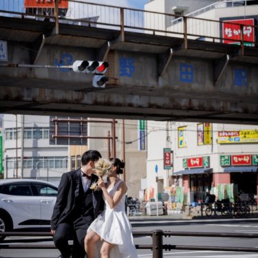 野田駅の高架下で、ドライフラワーのブーケで顔を隠してキスをする新郎とショート丈のドレスの花嫁の街ロケ前撮り