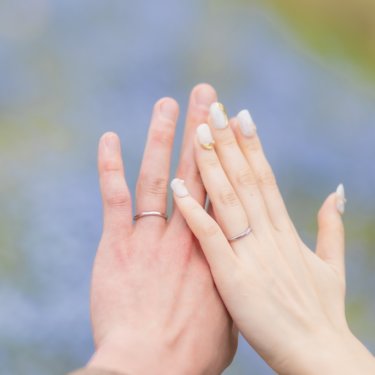 ネモフィラの花を背景に、手のひらを重ねて結婚指輪を見せる新郎新婦の手元。春の花畑で撮る前撮りのディテール