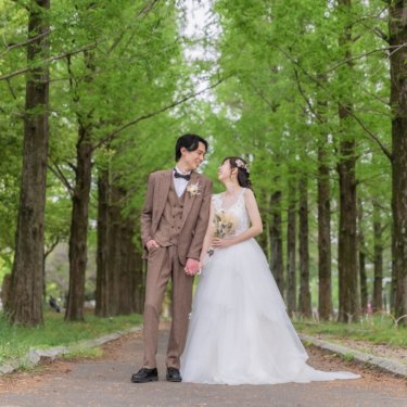 メタセコイア並木の小道で手をつなぎ、顔を見合わせるツイードの新郎とウェディングドレスの花嫁の洋装前撮り