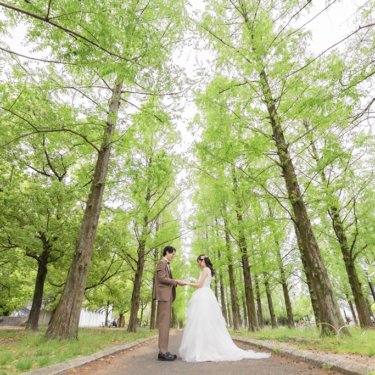 新緑のメタセコイア並木の小道で向き合い、手を取り合う新郎と花嫁を広く捉えた鶴見緑地公園のロケーションフォト