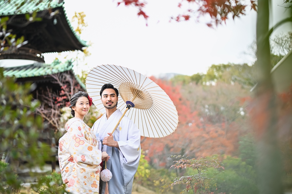 多宝塔のそばで白い和傘を差して笑い合う新郎新婦。色打掛と紋付袴で撮る紅葉の和装ロケーションフォト