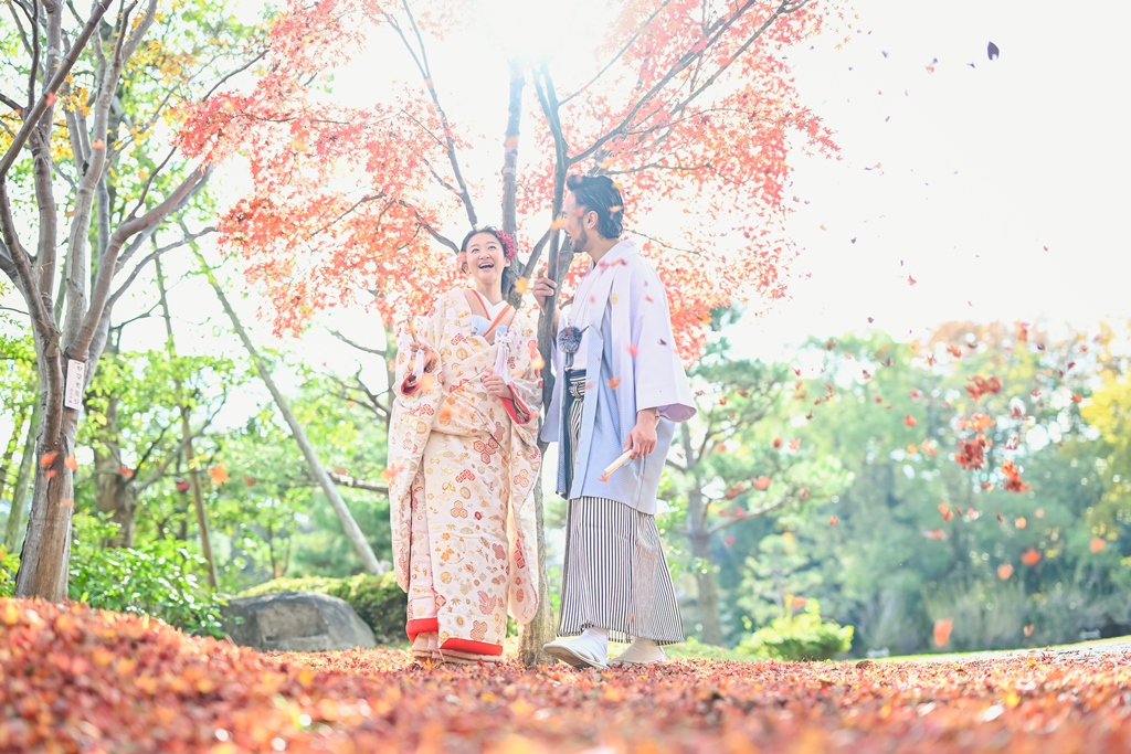 藤田邸跡公園の紅葉の落ち葉の上で見つめ合う色打掛の花嫁と羽織袴の新郎。色づく庭園での秋の和装前撮り