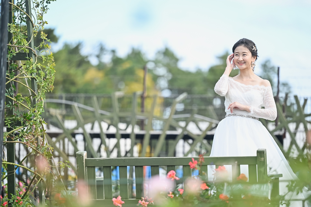 ばら庭園のベンチのそばで微笑む花嫁