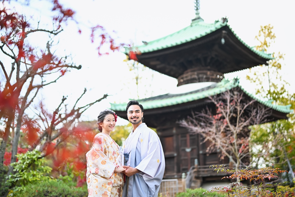 紅葉に囲まれた多宝塔を背景に寄り添う色打掛の花嫁と羽織袴の新郎。秋の和装前撮りのワンシーン