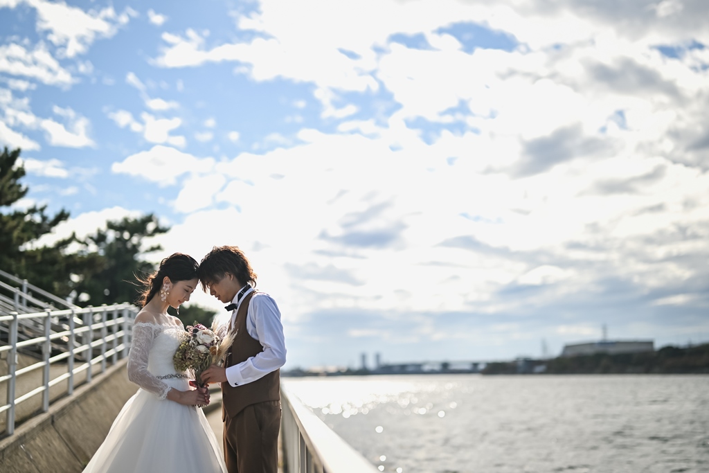 浜寺公園の海辺の遊歩道でおでこを寄せ合うウェディングドレスの花嫁とベスト姿の新郎のウェディングフォト