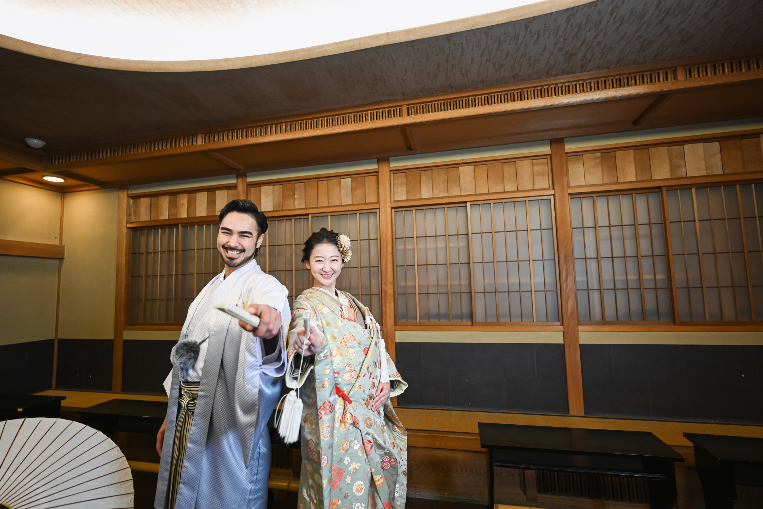 むらさき亭の縁側に座る花嫁と傍らに立つ新郎の和装ツーショット