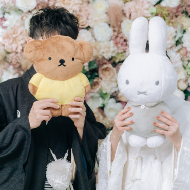 フラワーウォールの前でクマとウサギのぬいぐるみで顔を隠す紋付の新郎と白無垢の花嫁、遊び心のある和装前撮り