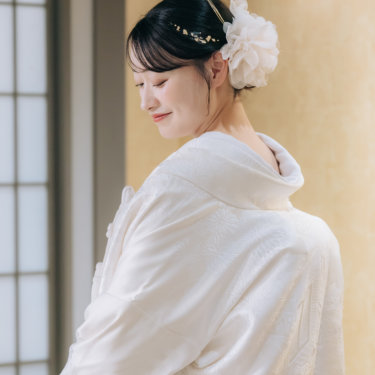 金色の壁を背に、大きな花の髪飾りをつけて目を伏せる白無垢の花嫁の後ろ姿のアップ。スタジオ和装前撮り
