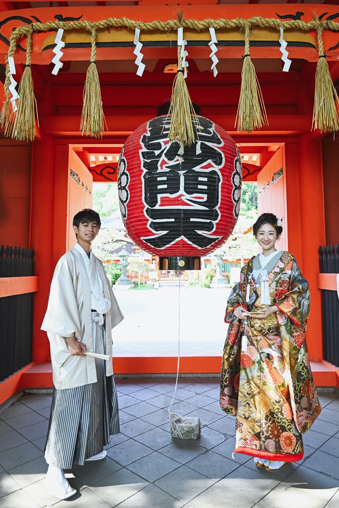 毘沙門堂の朱塗りの門に下がる大提灯の下に並ぶ、色打掛の花嫁と白い羽織袴の新郎の和装前撮り