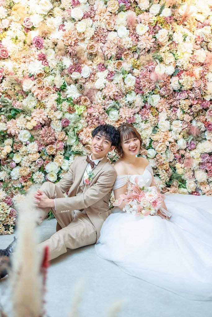 フラワーウォールの前に座るベージュスーツの新郎と白ドレスの花嫁|家族やペットと叶えるフォトウェディング