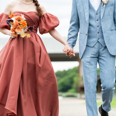 手をつないで並んで歩く、テラコッタドレスの花嫁とライトブルースーツの新郎。腰から下の構図でとらえたウェディングフォト