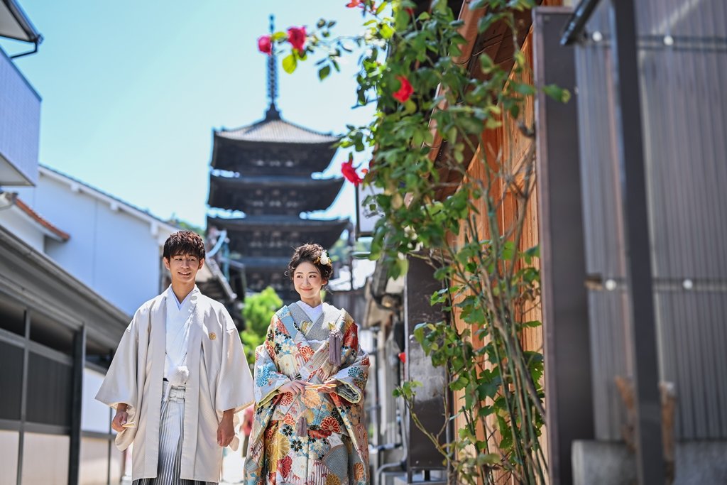 八坂の塔がそびえる京都の路地を歩く、生成り色の着物袴の新郎と色鮮やかな花柄着物の花嫁