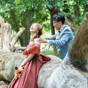 倒木に腰掛けて声をあげて笑う花嫁と、その肩に手を添えて見つめる新郎。森の中での自然体なウェディングフォト