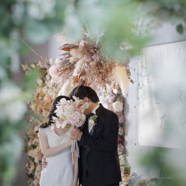 ドライフラワーの装花の前で、ブーケに隠れてくちづけを交わす新郎新婦。ナチュラルなスタジオフォト
