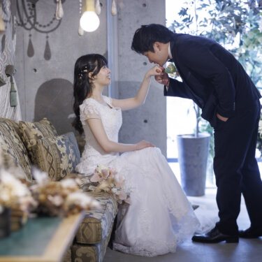 アンティークソファに腰掛けた花嫁の手にくちづける新郎。大阪のスタジオでの洋装前撮り