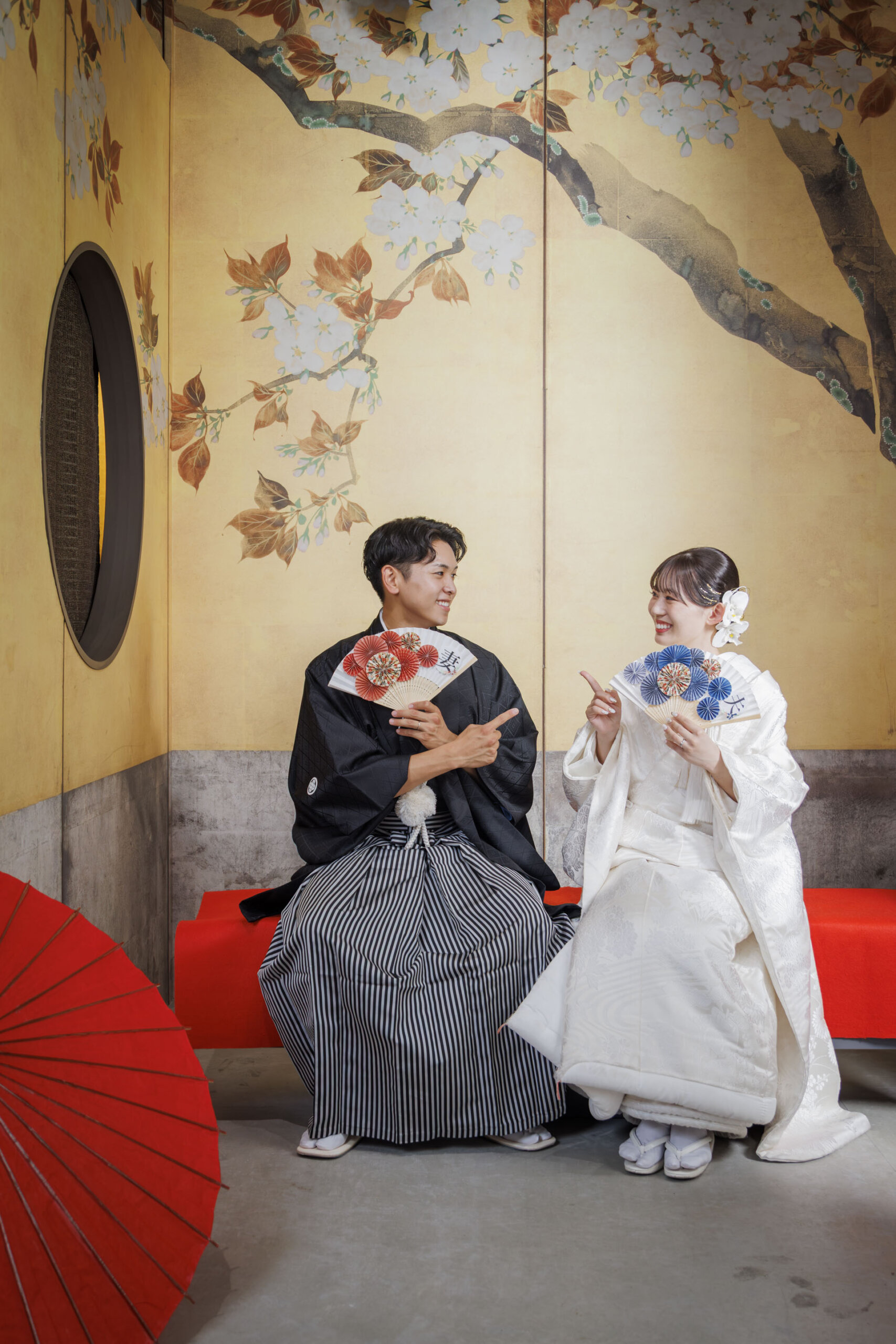 金屏風×桜柄セットで扇子を持ちポーズをとる新郎新婦