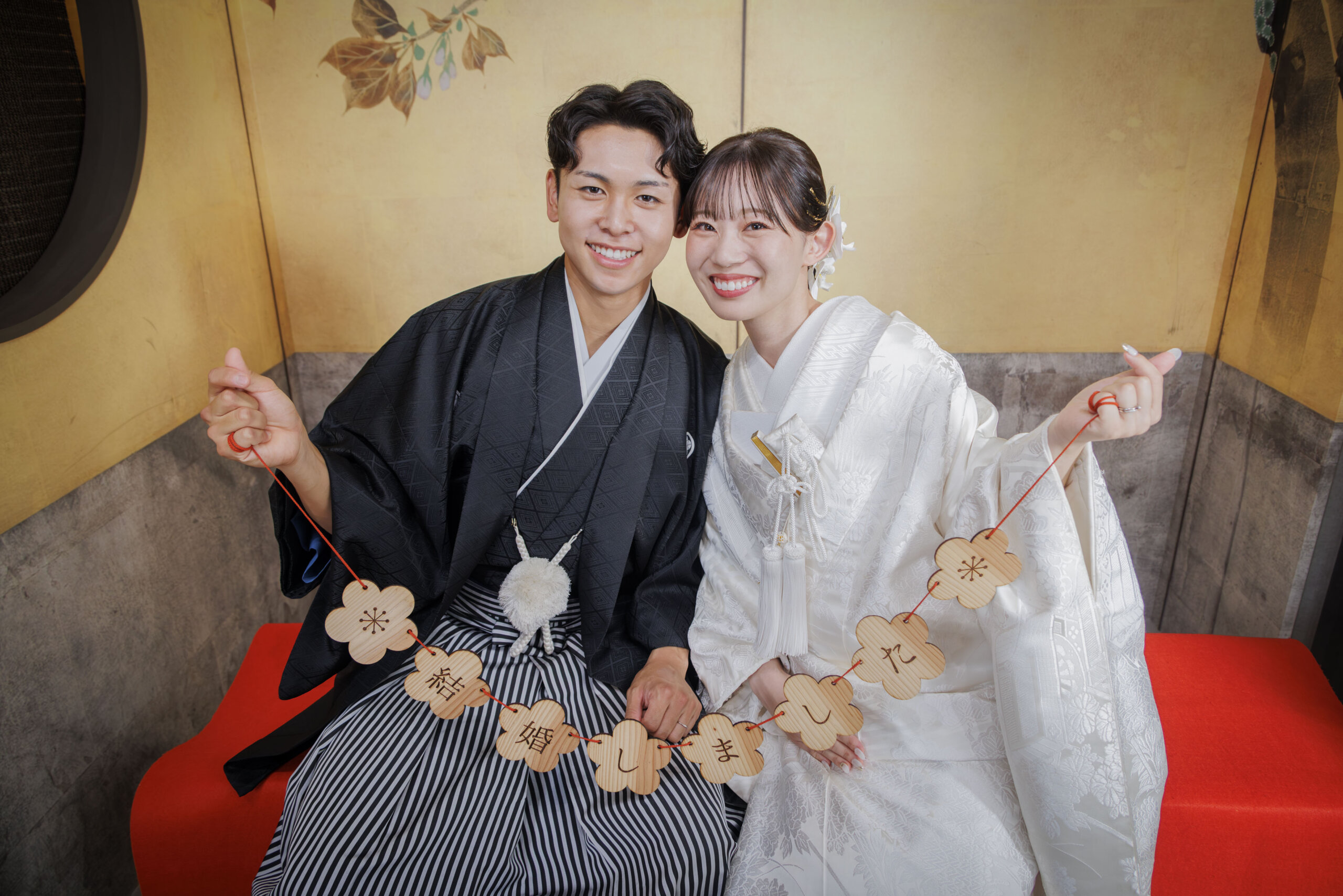 金屏風のセット前で「結婚しました」の木製プレートを掲げる新郎新婦