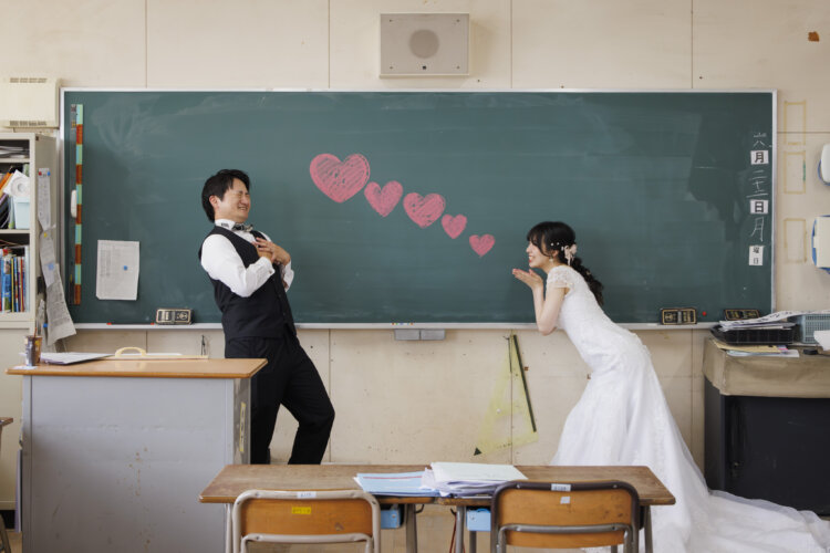 黒板に描いたハートを投げる花嫁と、胸に受け止める新郎。遊び心のある教室でのウェディングフォト