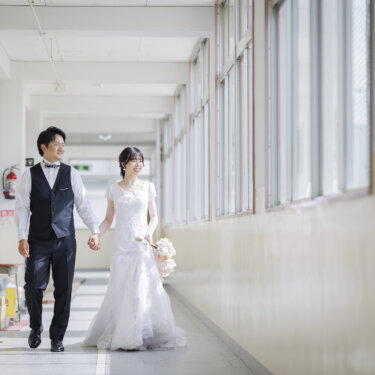 学校の廊下を手をつないで歩くベスト姿の新郎とウェディングドレスの花嫁。学校ロケーションで撮る洋装前撮りの廊下カット