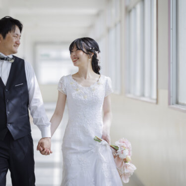 光が差し込む学校の廊下を、手をつないで歩く新郎新婦。思い出の校舎で撮るフォトウェディング