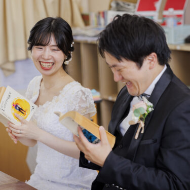 教室の机で本を開き、声をあげて笑い合う新郎新婦。学校ロケーションフォトのひとこま
