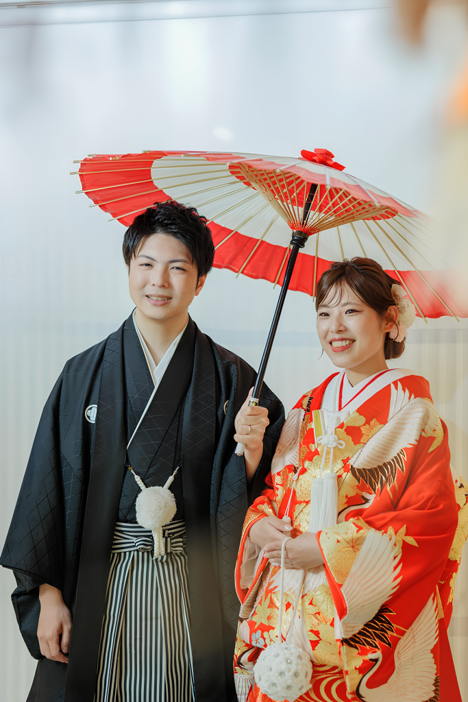 髪飾りを添えた和装で紅白の和傘を差す新郎新婦