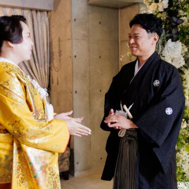 シャンデリアの下で手を合わせて話しかける色打掛の花嫁と、笑顔で応える紋付袴の新郎。心斎橋店のスタジオフォト