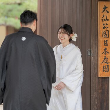 大仙公園日本庭園の門の前で、新郎と向き合って笑う白無垢の花嫁。木札が入る記念の和装前撮り