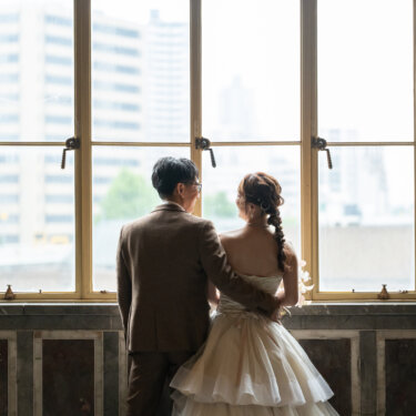 大阪中央公会堂の窓辺に並び、外の景色を眺める新郎新婦の後ろ姿を写したロケーションフォト