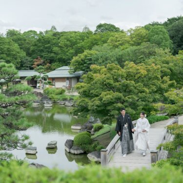 松と池が広がる大仙公園日本庭園を見下ろし、石橋を渡る新郎新婦を遠景で写した和装ロケーションフォト