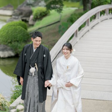 池にかかる木の反り橋のたもとで手をつなぐ、白無垢の花嫁と紋付袴の新郎。日本庭園で撮る結婚写真