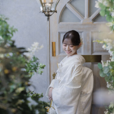 アンティーク調の扉とランプの前で、うつむいて微笑む白無垢の花嫁のソロショット。心斎橋店のスタジオでの前撮り